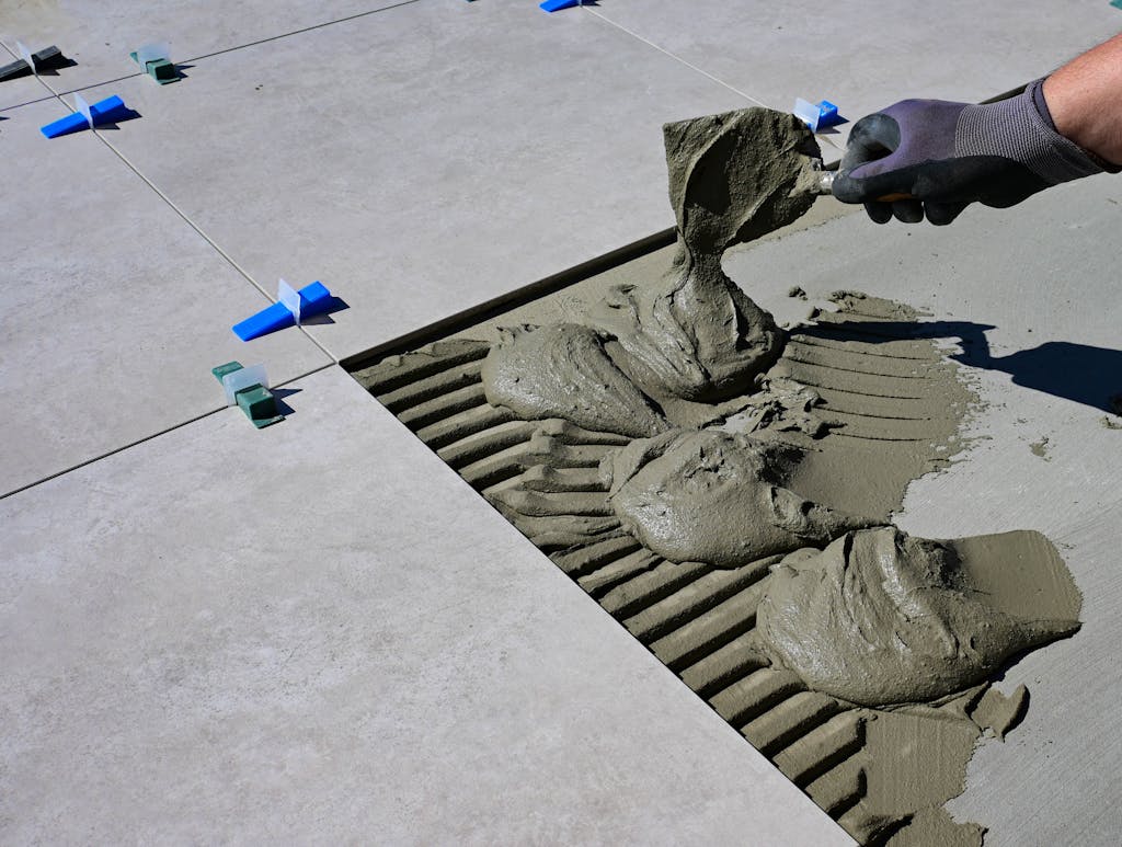 Close-up of a gloved hand applying mortar for ceramic tile installation outdoors.